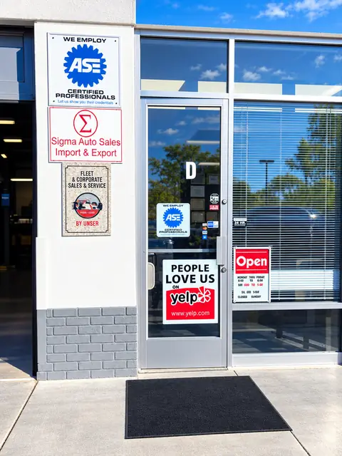 Glass customer entrance door at Jim's Automotive with posted signs, a Yelp People Love Us sticker and an Open sign
