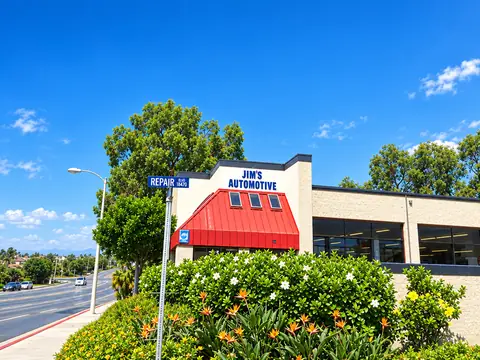 Street-level view of Jim's Automotive behind flowering landscaping, with the Repair Ln street sign at left, Huntington Beach
