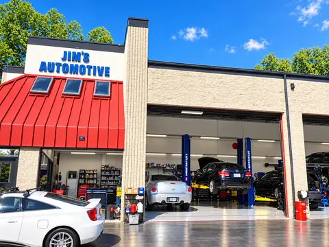 Front of Jim's Automotive in Huntington Beach with roll-up service bay doors open and cars raised on lifts inside