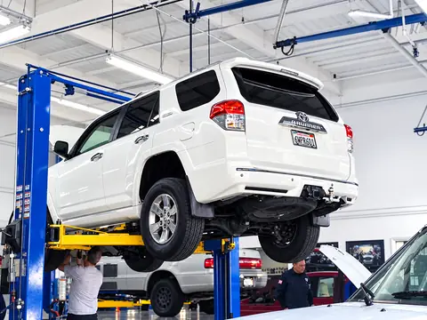 White SUV raised on a blue two-post lift for undercarriage service at Jim's Automotive in Huntington Beach