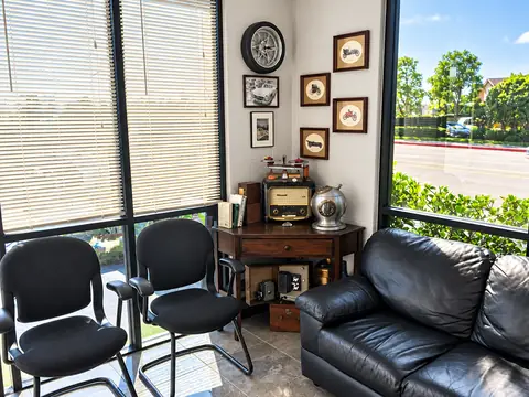 Waiting area at Jim's Automotive with chairs, a leather sofa, a wall clock and framed pictures beside a sunny window