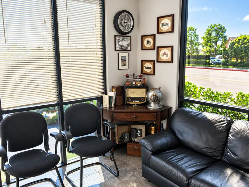 Waiting area at Jim's Automotive with chairs, a leather sofa, a wall clock and framed pictures beside a sunny window